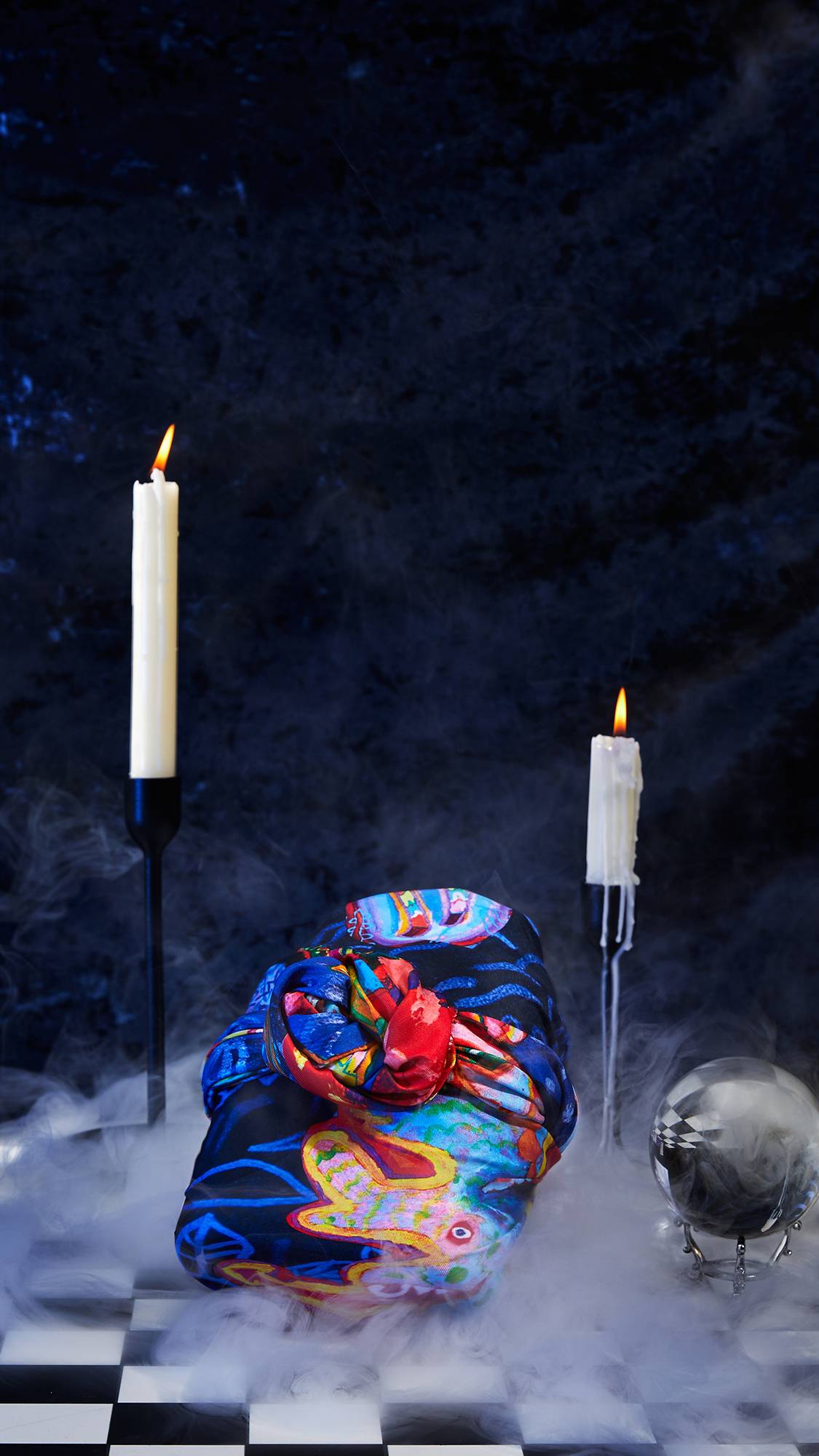 The image shows the Fantasy Animals knot wrap neatly tied around an unknown gift. It is surrounded by two pillar candles and a crystal ball on a stand. There is a dark, velvet background.