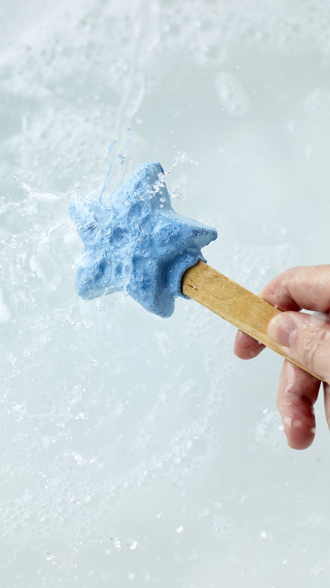 The image shows a close-up shot of the Frozen reusable bubble bar stick being held under running tap water. The icy-blue star at the end creates bubbly, cool-blue water below.