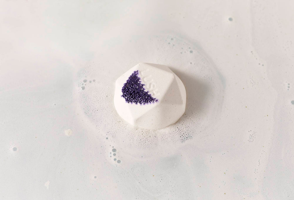 Fuurin bath bomb sits on calm, silky, white water with purple-coloured salt and "Lush" embossed on top.