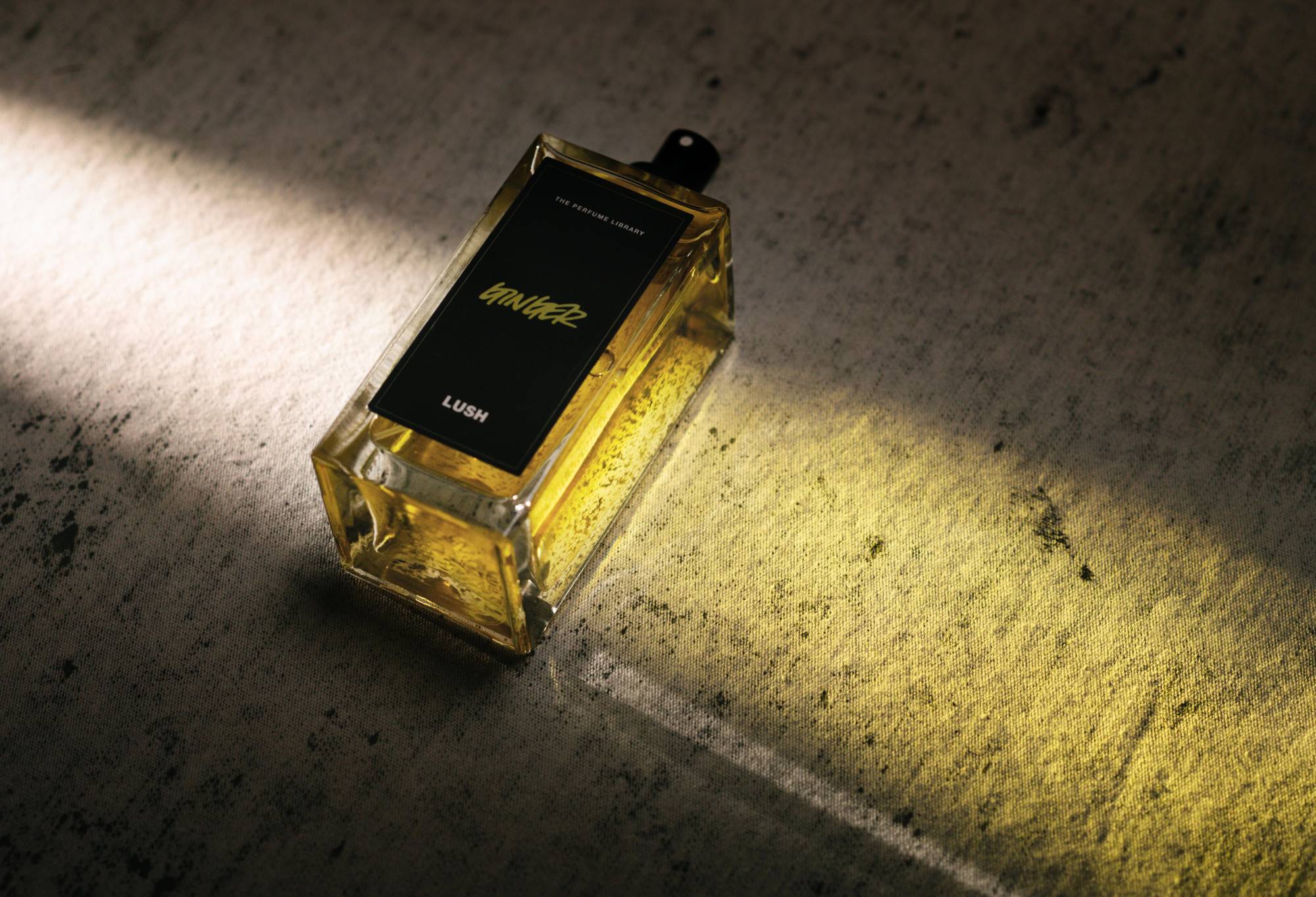 Ginger, a bottled, black label perfume, lies flat, with light shining through it, creating a pale golden cast of light.