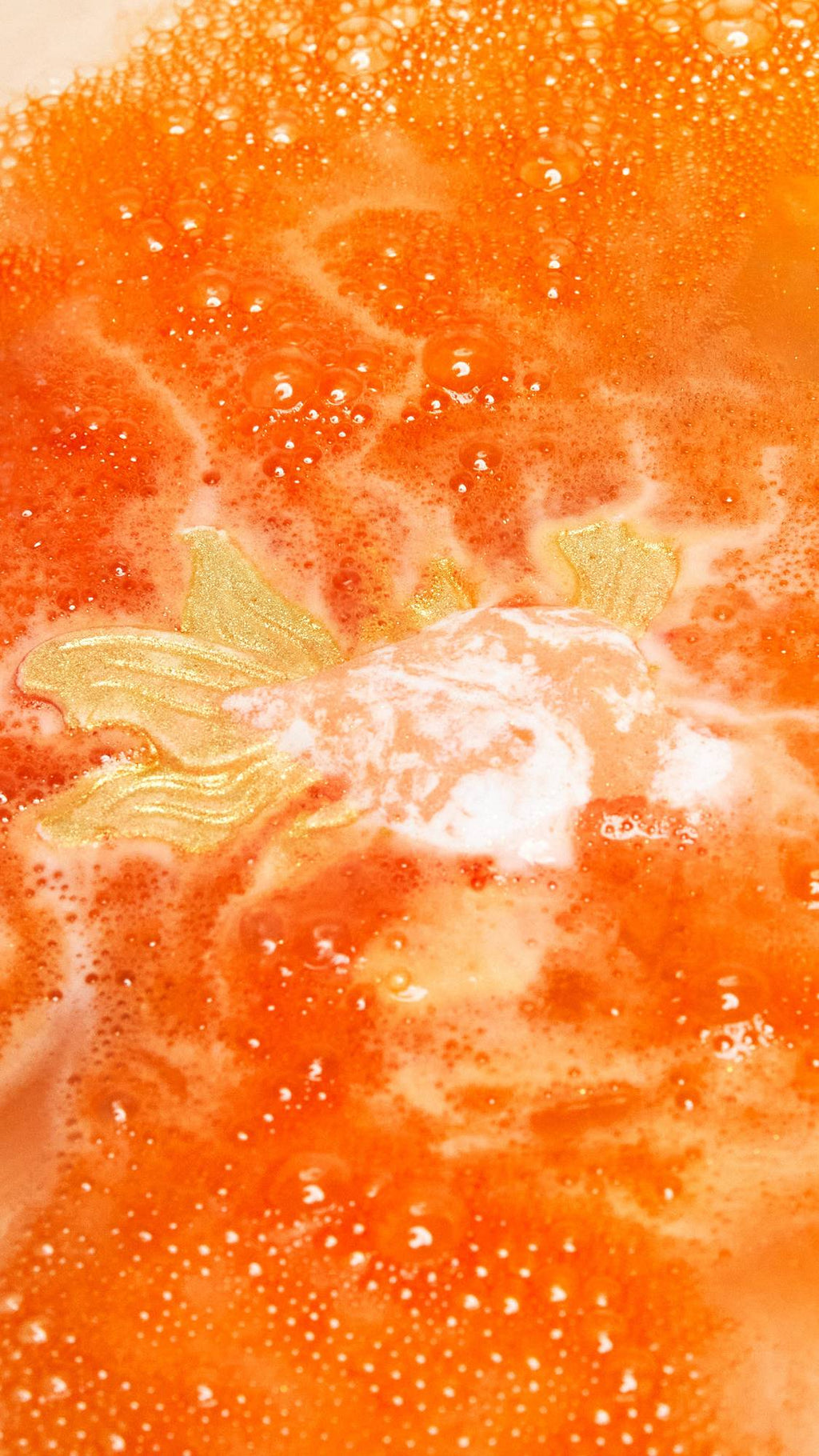 The Goldfish bath bomb is slowly dissolving creating a shimmering sea of deep, sunset-orange water and thick, vibrant foam.