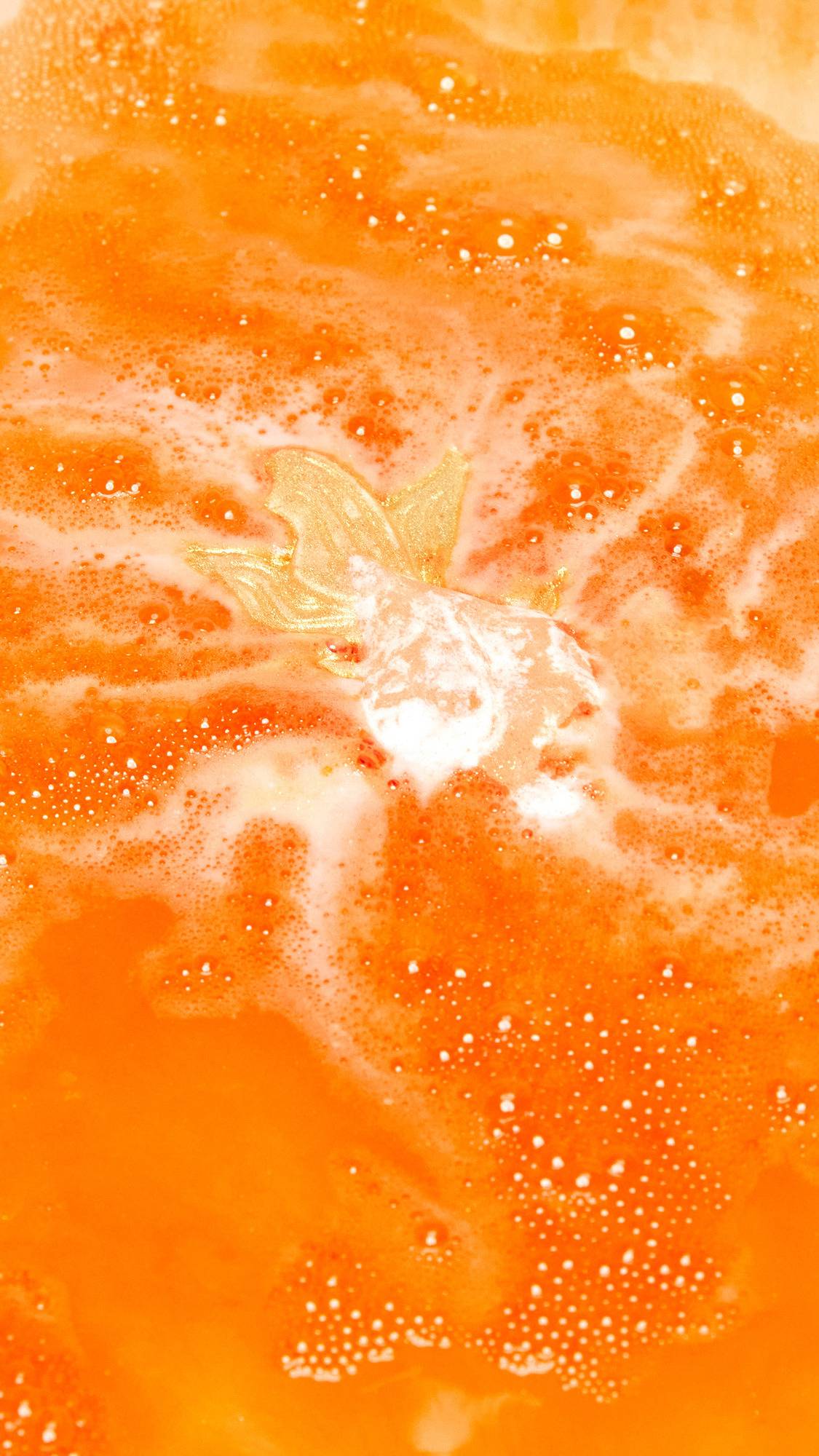 The Goldfish bath bomb is slowly dissolving creating a shimmering sea of deep, sunset-orange water and thick, vibrant foam.