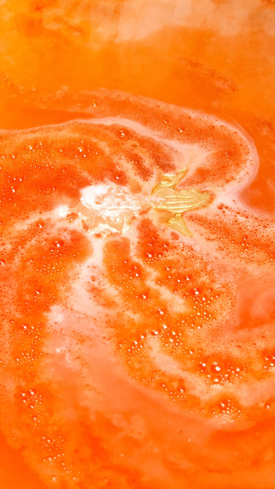 The Goldfish bath bomb is slowly dissolving creating a sea of deep, sunset-orange water and thick, vibrant foam.