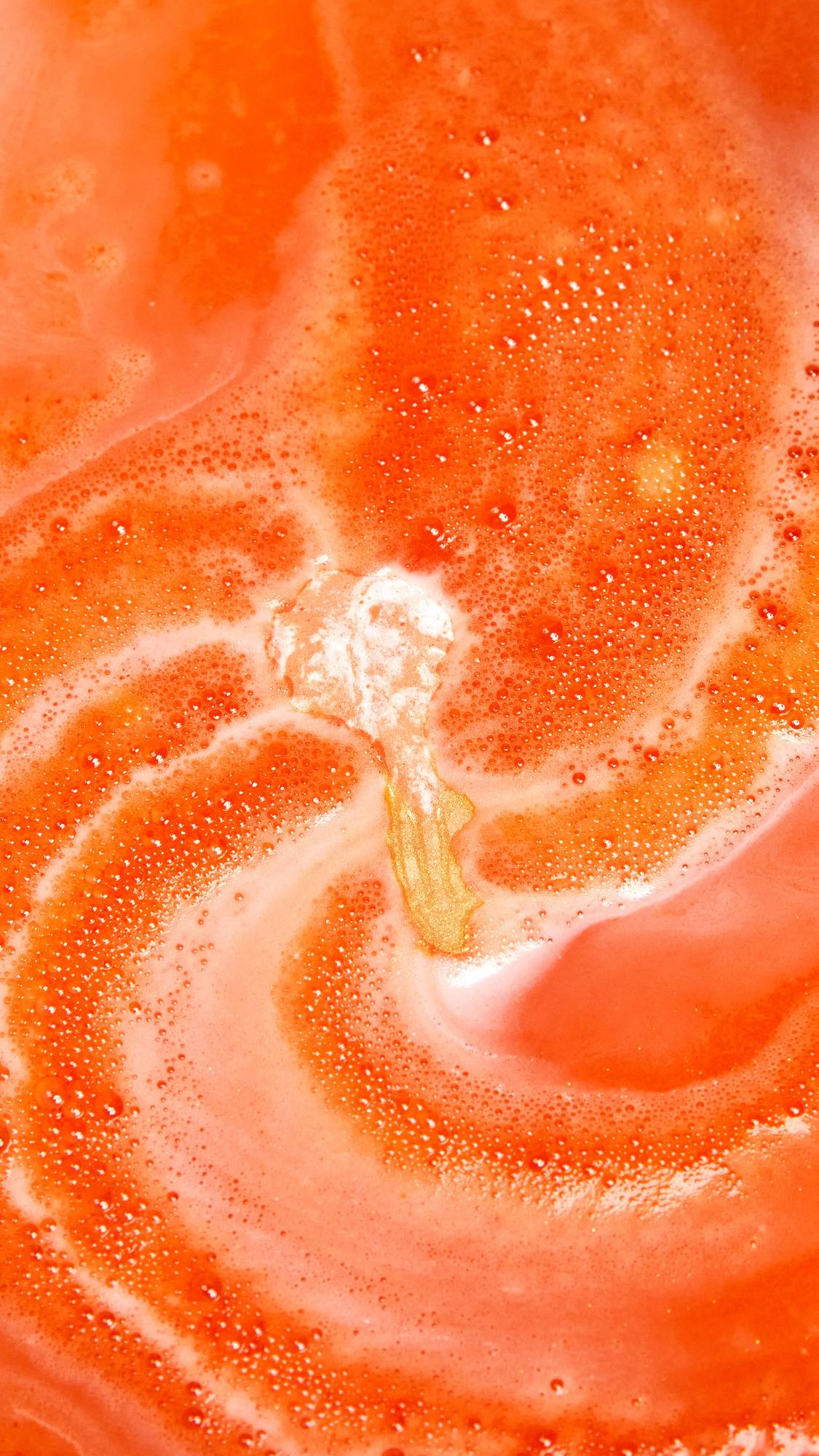 The Goldfish bath bomb is slowly dissolving creating a sea of deep, sunset-orange water and thick, vibrant foam.