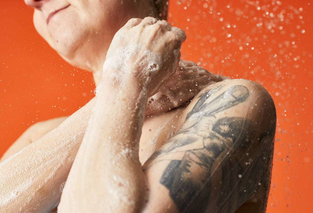 A person lathers up their neck with their hands, while in front of a bright orange background.