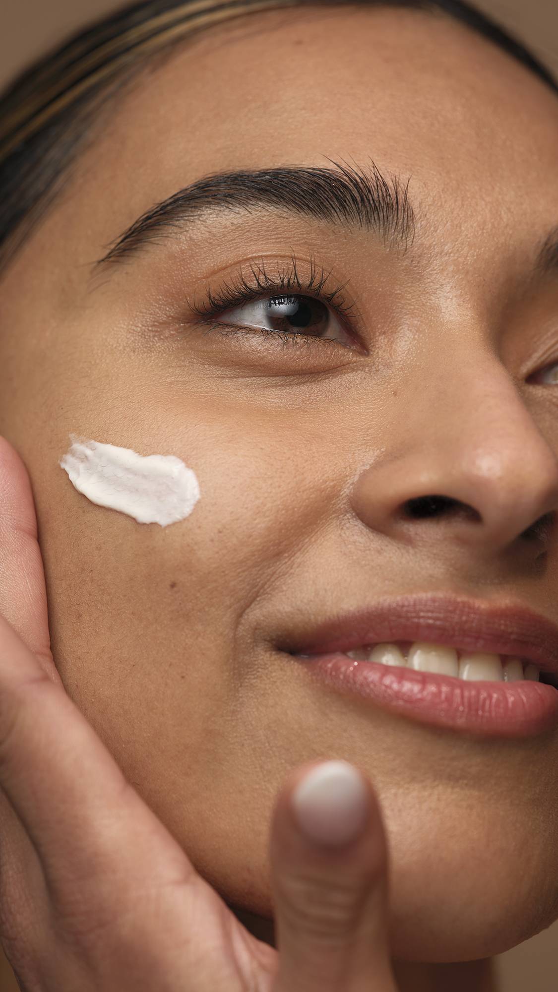 A super close-up of the model's side of their face smiling widely as they smooth the Gorgeous self-preserving moisturiser over their cheek.