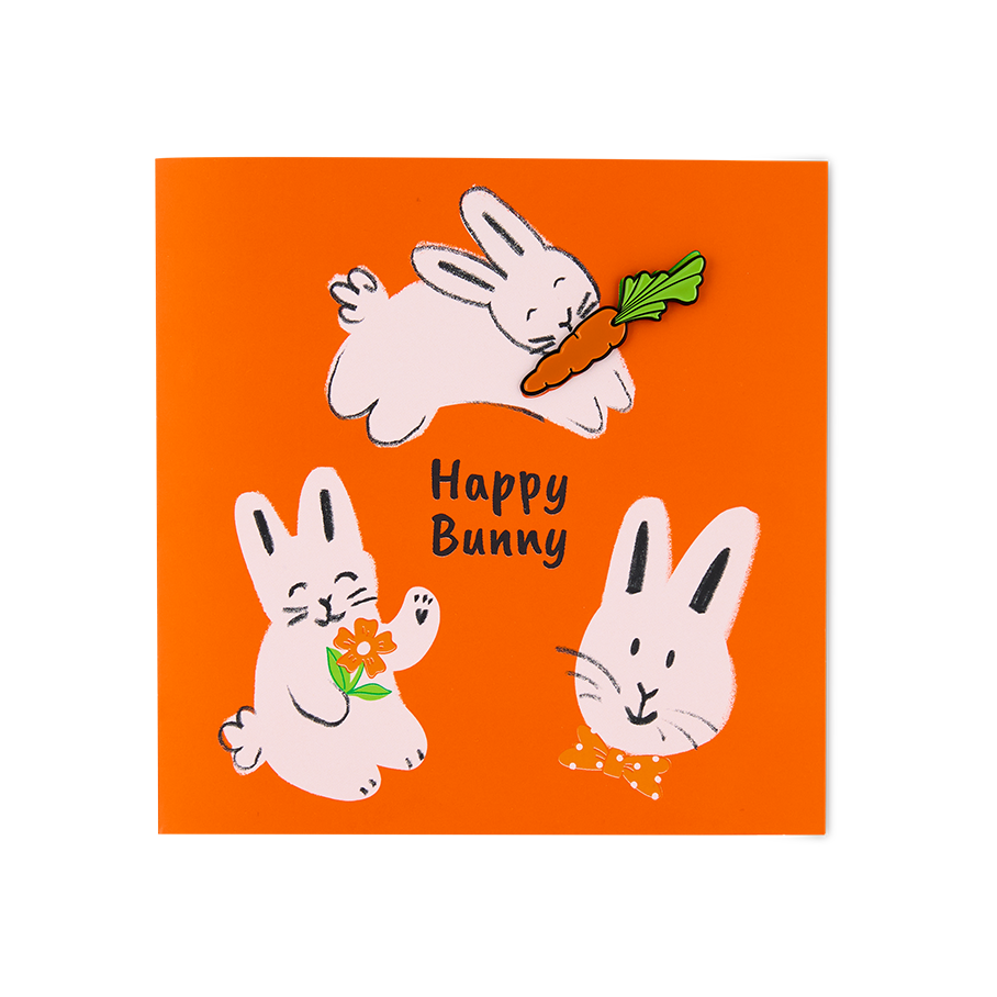 Happy Bunny. An orange greeting card features three hand-drawn pink rabbits and the text "Happy Bunny". One rabbit carries a carrot, another holds an orange flower, and a third wears a polka-dot bow tie. The carrot is a removable pin badge.