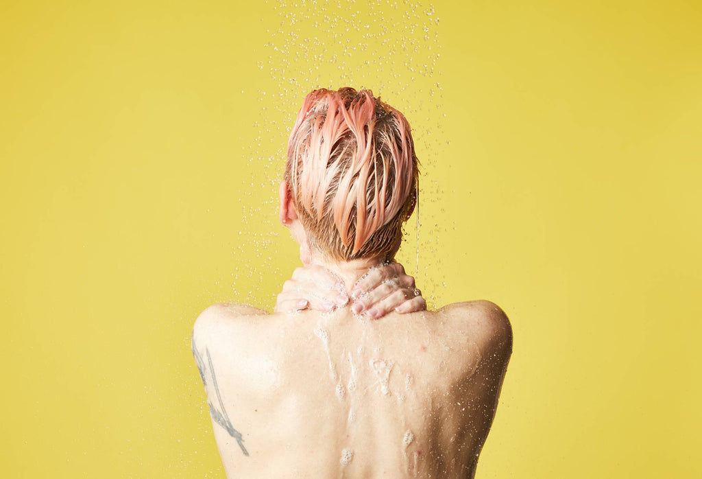 A model stands with upper back and head shown, lather running down from hands over their neck, in front of a yellow background.