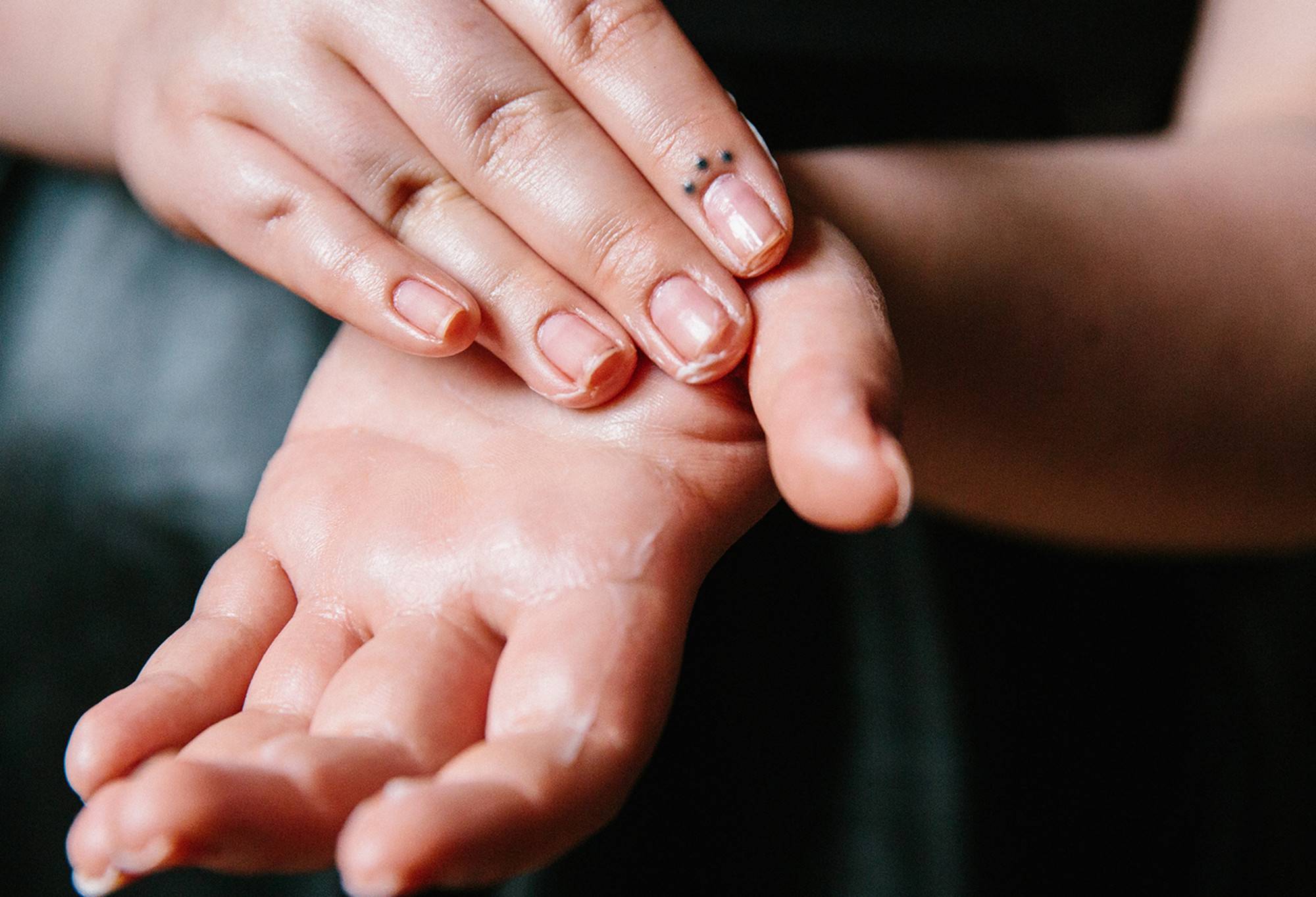 Helping Hands, a pale pink hand cream, is being rubbed into the upturned palm of one hand by the fingers of the other.