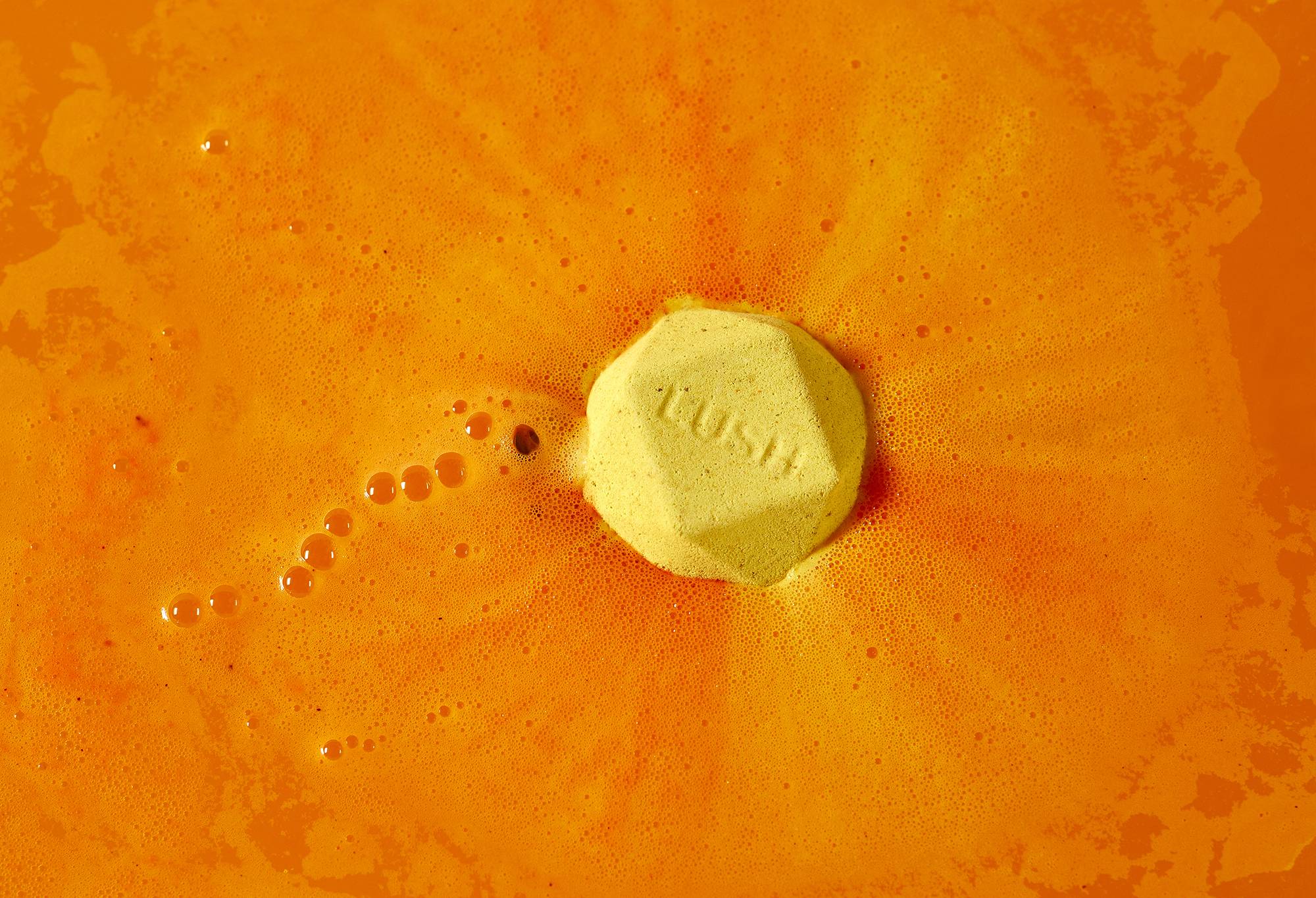 Hinata bath bomb. Bright yellow bath bomb sits among electric orange, silky foam.