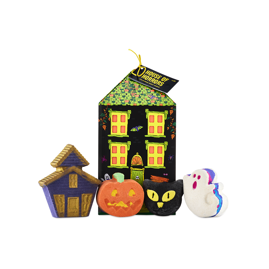 A Lush 'House of Horrors' gift. A house-shaped box stands behind four Halloween-themed bath products: a purple haunted house, an orange pumpkin, a black cat head, and a white ghost with blue and pink edges.