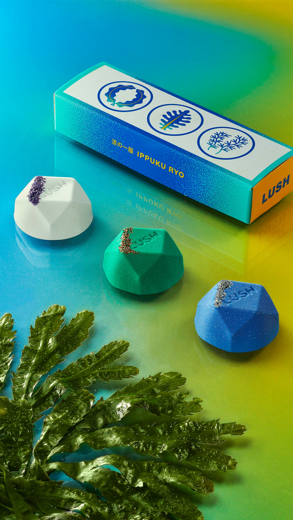 Three Ippuku cooling bath bombs in a line with seaweed on the left, and the box on the right on top of a blue-to-green gradient.