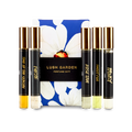 The image shows a "LUSH GARDEN" perfume gift set. Five thin, cylindrical glass perfume bottles with amber and clear liquids are arranged around a dark blue box featuring a large white floral design.