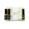 The image shows a "LUSH Triptych" perfume gift set. Three thin, cylindrical glass perfume bottles with amber and clear liquids are arranged around a pale yellow and green marbled box with a white band.