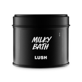 A matte black circular tin with a matching lid. The front label features the Lush logo and the product name "Milky Bath" in bold, white hand-drawn style typography. Set against a plain grey background.