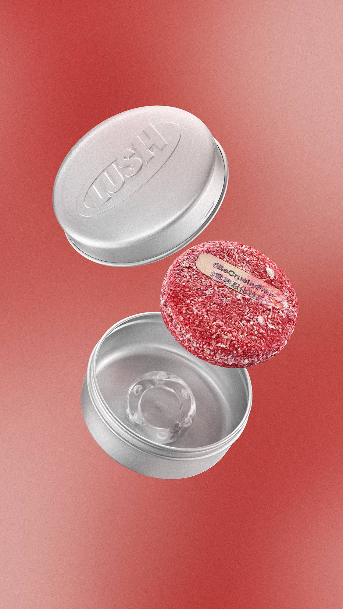 Floating against a warm red gradient, a textured red circular "NEW" shampoo bar with a small wooden tab is shown alongside an open, silver aluminium tin and its lid, which is embossed with the 'LUSH' logo.