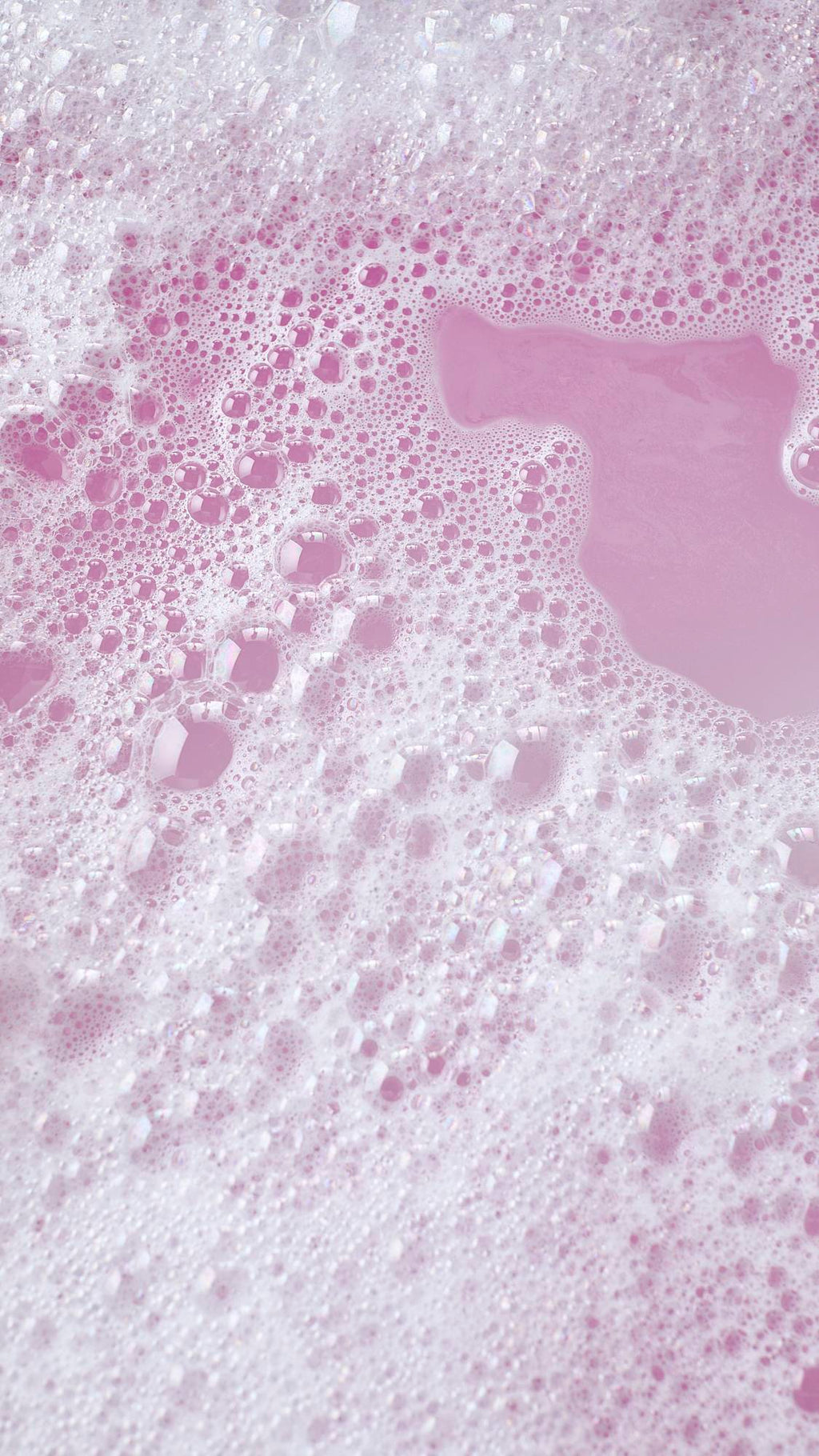 The image shows the colourful aftermath of using the Pink Flamingo reusable bubble bark stick. There is delicate, rose-pink bath water surrounded by mountains of bright bubbles.