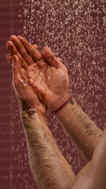 A close-up image of the model's hands under running shower water on a chocolate-coloured background. They are foaming up the caramel-chocolate-coloured Posh Chocolate shower gel in their hands to create a rich lather
