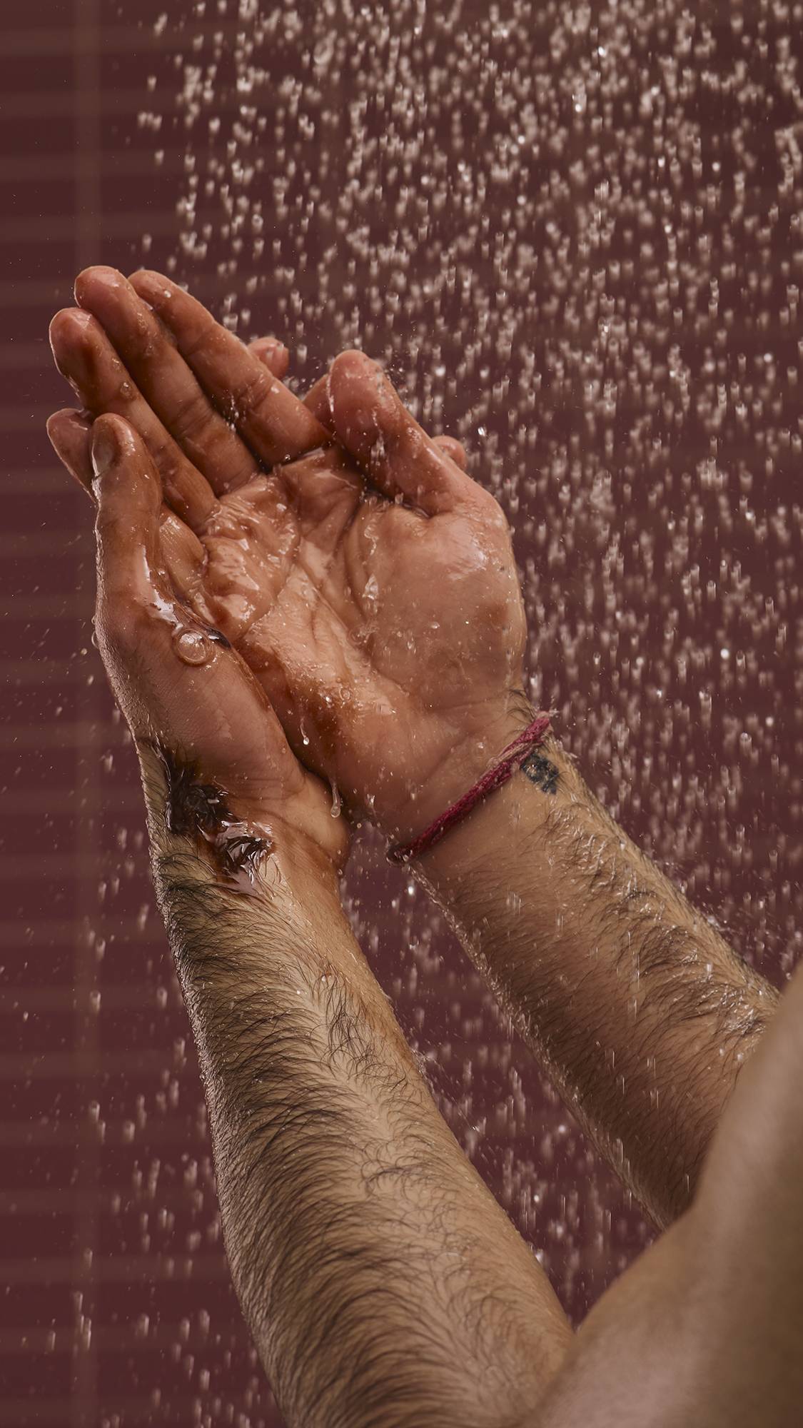 A close-up image of the model's hands under running shower water on a chocolate-coloured background. They are foaming up the caramel-chocolate-coloured Posh Chocolate shower gel in their hands to create a rich lather