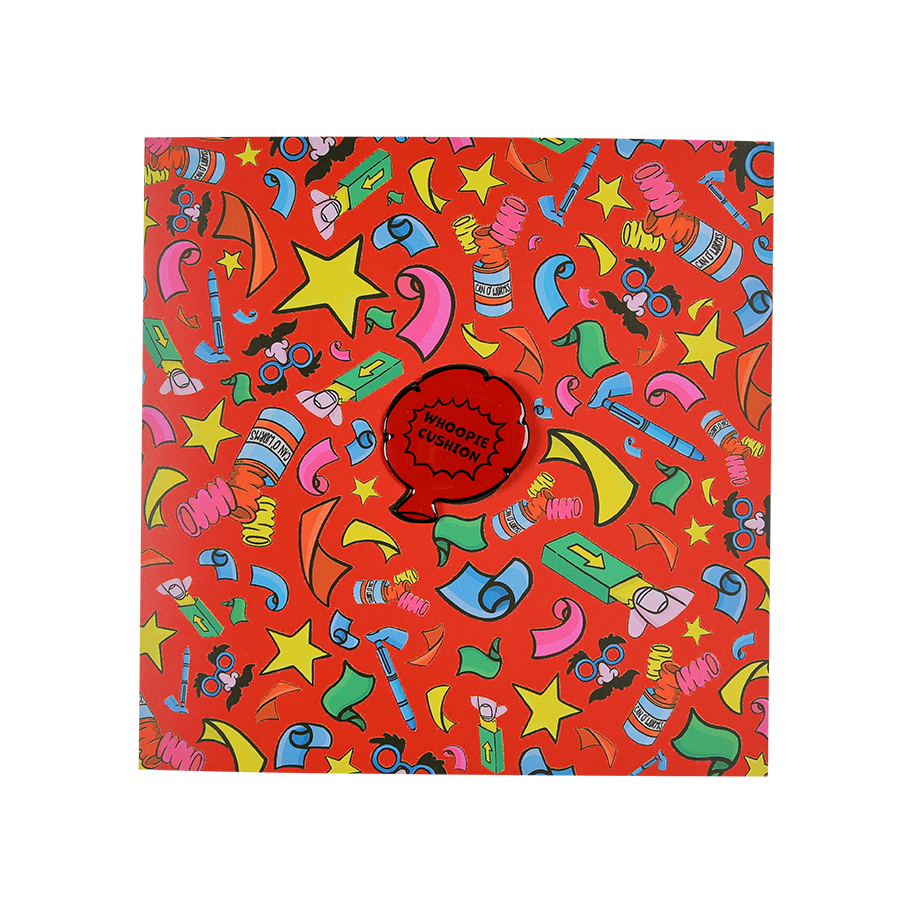 Practical Joker. A square greetings card with a bright red background. The card has illustrations of accessories associated with practical jokes including false gum and confetti. In the centre is a detachable, red, whoopee cushion pin badge.