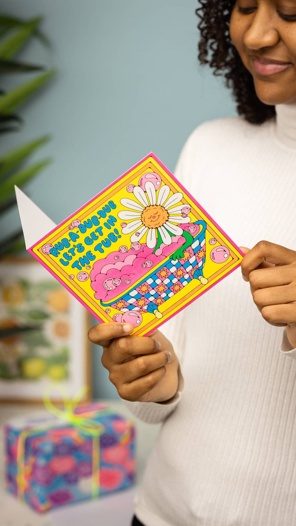 Image shows the model reading the Rub-A-Dub-Dub Let's Get In The Tub card with a gift in the background.
