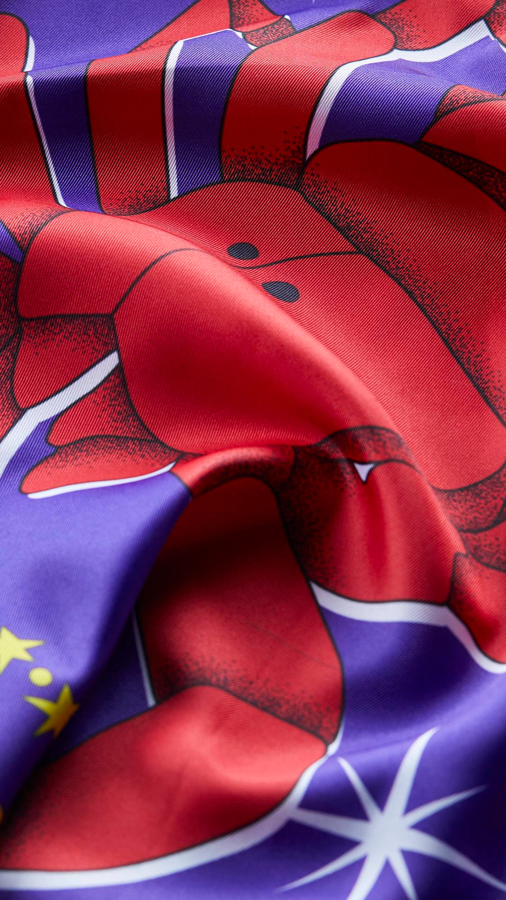 The image shows a super close-up of the Scorpio knot wrap as it lays ruched. The image focuses on the texture of the fabric and the vibrant contrasting colours of reds and purples.