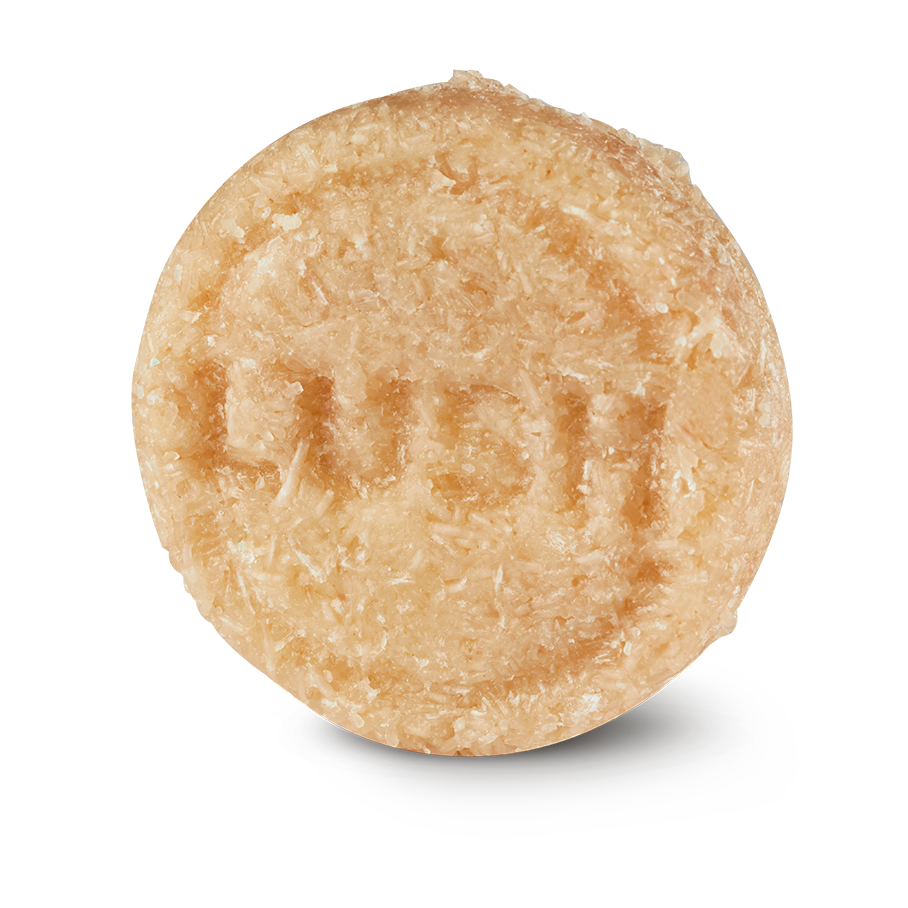 Honey I Washed My Hair. A round, textured, pale beige Lush solid shampoo bar. The bar has a rough, shredded-coconut texture and is embossed with the "LUSH" logo in the centre.