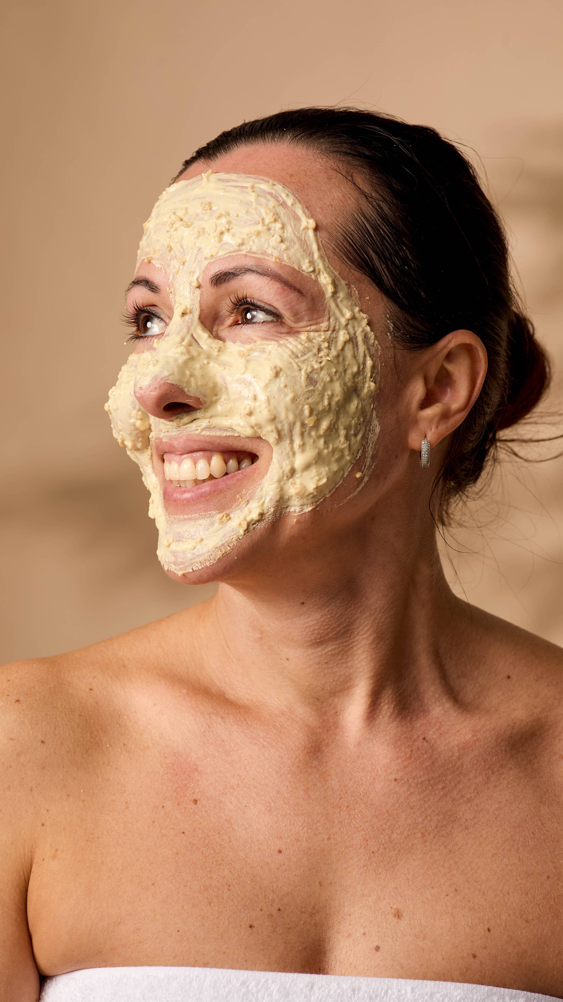 The model is smiling into the distance surrounded by warming light as their face is evenly coated in the Skin Soothing Porridge.