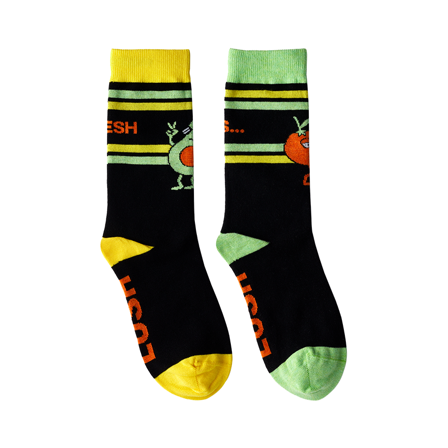 Fresh Values. Black socks with the toe, heel and top striped with bright yellow and green. Socks have an avocado and tomato on.