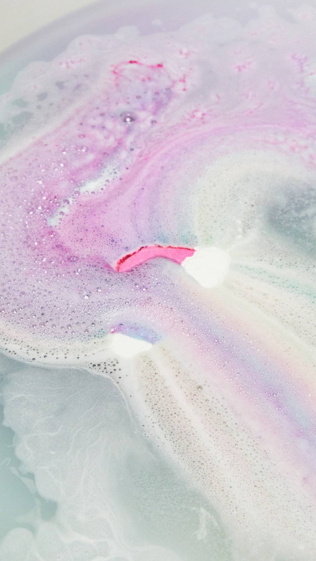 The Somewhere bath bomb is slowly dissolving leaving behind delicate, pink and blue pastel waters with thin velvety foam.