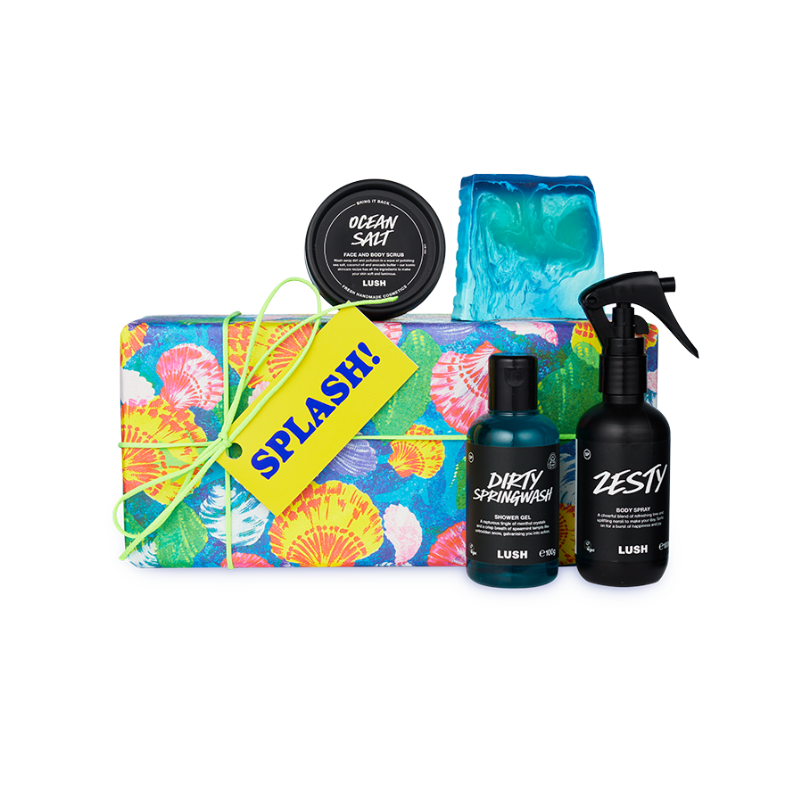 Splash! A gift box wrapped in colourful shell-patterned paper and tied with green string. Four LUSH products including a soap, body spray, body scrub and shower gel sit around and on top of the box.