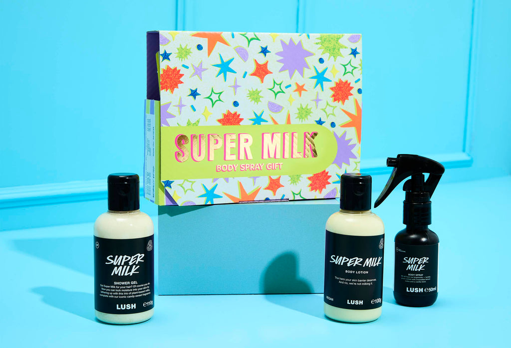 The Super Milk Body Spray Gift set sits on a blue surface. A colourful star-patterned box stands behind bottles of Shower Gel, Body Lotion, and Body Spray.
