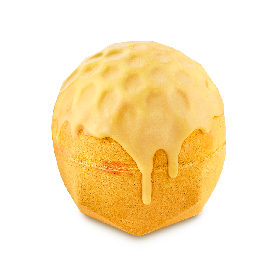Sweet As Honey. A spherical, golden-yellow bath bomb with a faceted, flat base. It has a honeycomb-textured top that appears to be melting or dripping down the sides like thick honey.
