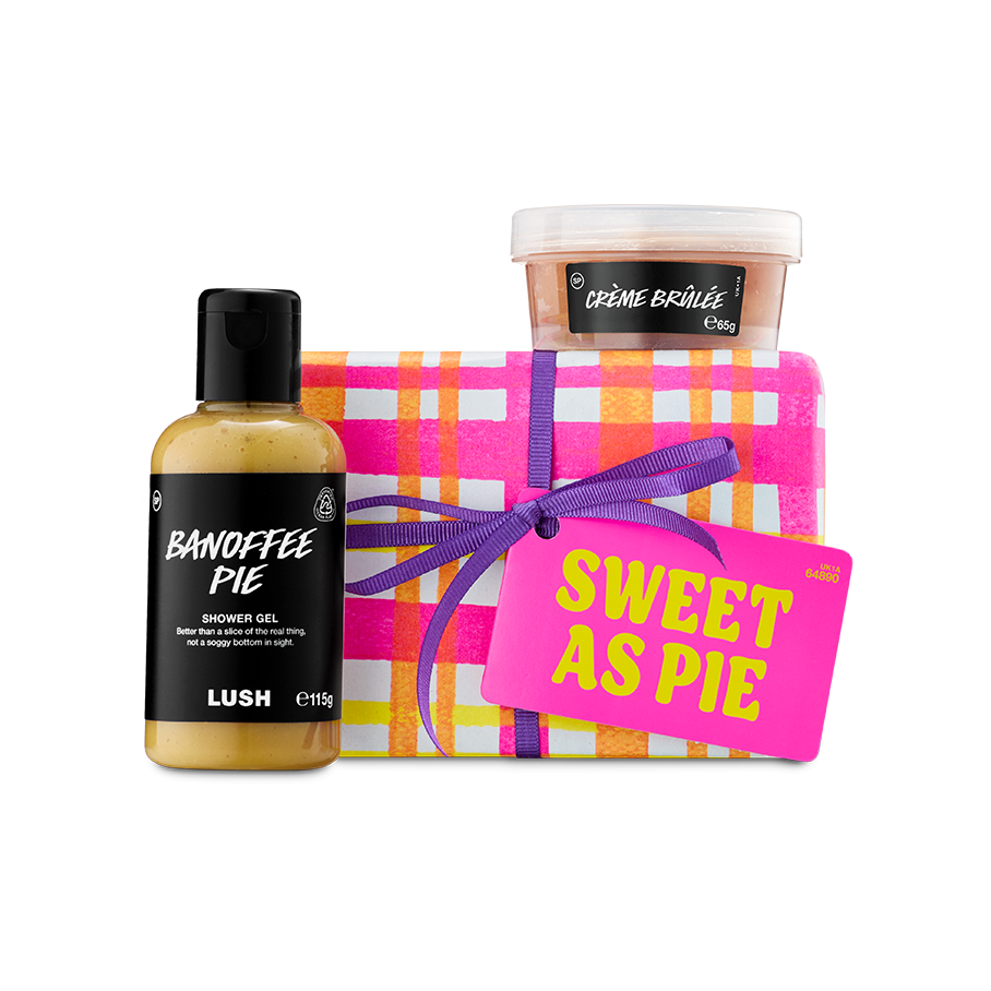 Sweet As Pie. A Lush gift set featuring a box wrapped in pink, orange, and white checked paper with a purple ribbon. It is presented with a bottle of Banoffee Pie shower gel and a pot of Crème Brûlée body scrub.
