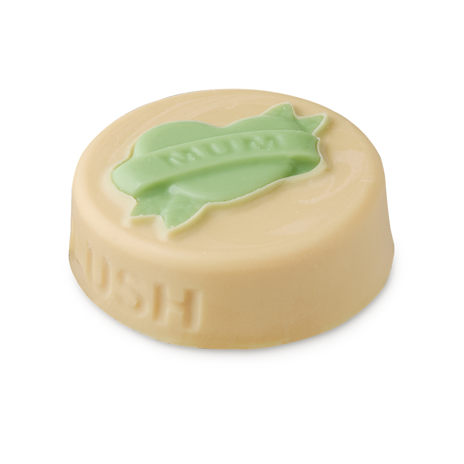 Symbol of Love. A flat, circular, ivory-coloured solid balm with the word LUSH embossed on the side. On top is a pale green heart with a ribbon across which reads "MUM".