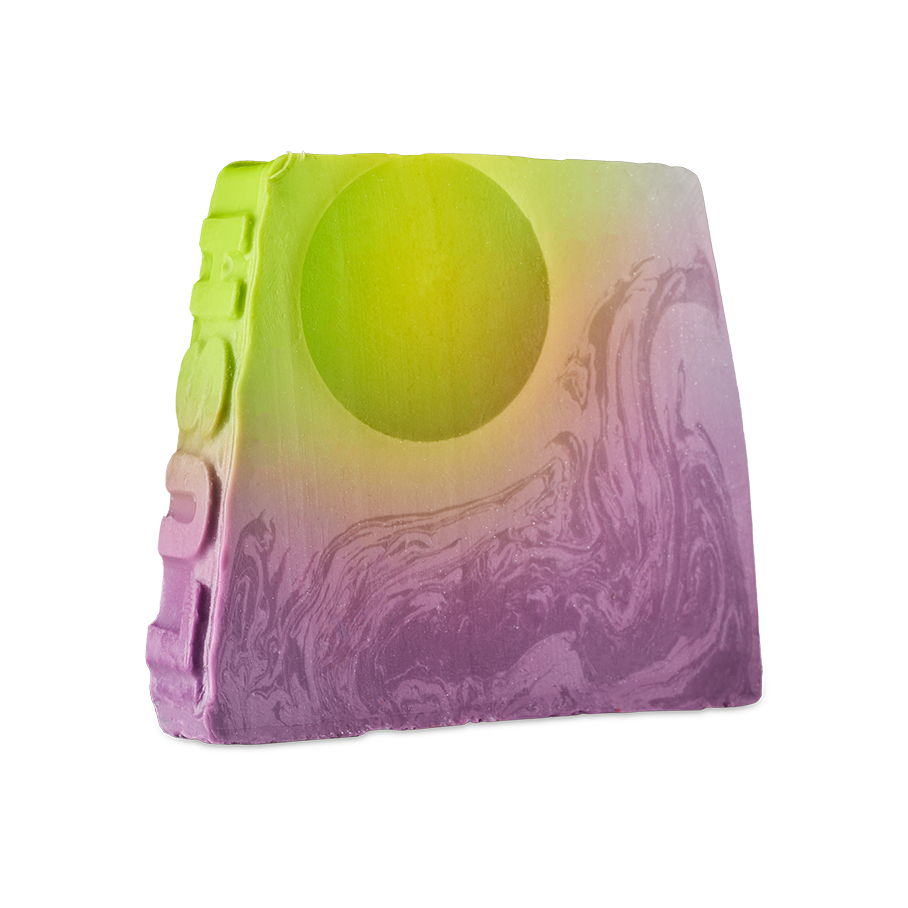 To The Moon and Back. An off-square slice of soap with a sunset-inspired design. The top features a lime green circle, resembling a sun, which gradients into a swirling, marbled purple base. The word "LUSH" is embossed vertically down the side.