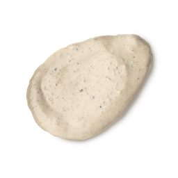 Tiny Musicians Of The Forest. A neatly smeared swatch of creamy, beige-coloured face mask with small dark exfoliating particles. The texture is rich and slightly lumpy, presented as a single dollop.