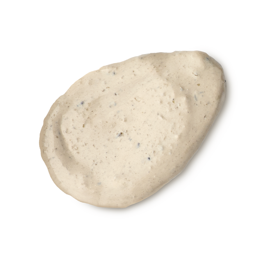 Tiny Musicians Of The Forest. A neatly smeared swatch of creamy, beige-coloured face mask with small dark exfoliating particles. The texture is rich and slightly lumpy, presented as a single dollop.