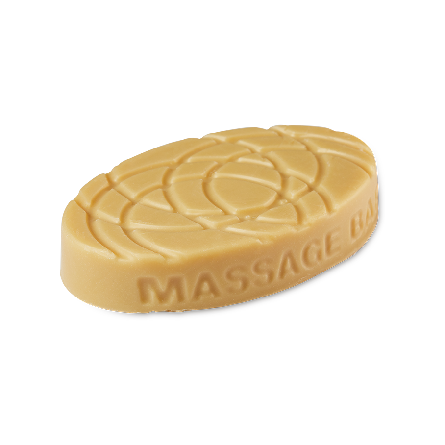 An oval, smooth caramel-coloured Lush "Turmeric Latte" massage bar features a geometric, indented pattern across its top surface. The words MASSAGE BAR are embossed along the curved edge.