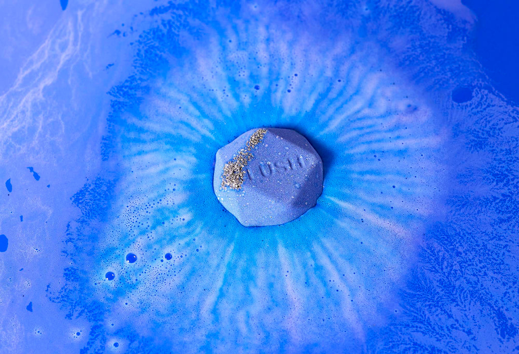 Uchumizu bath bomb floats among deep blue swirls with blue-coloured sugar and "Lush" embossed on top.