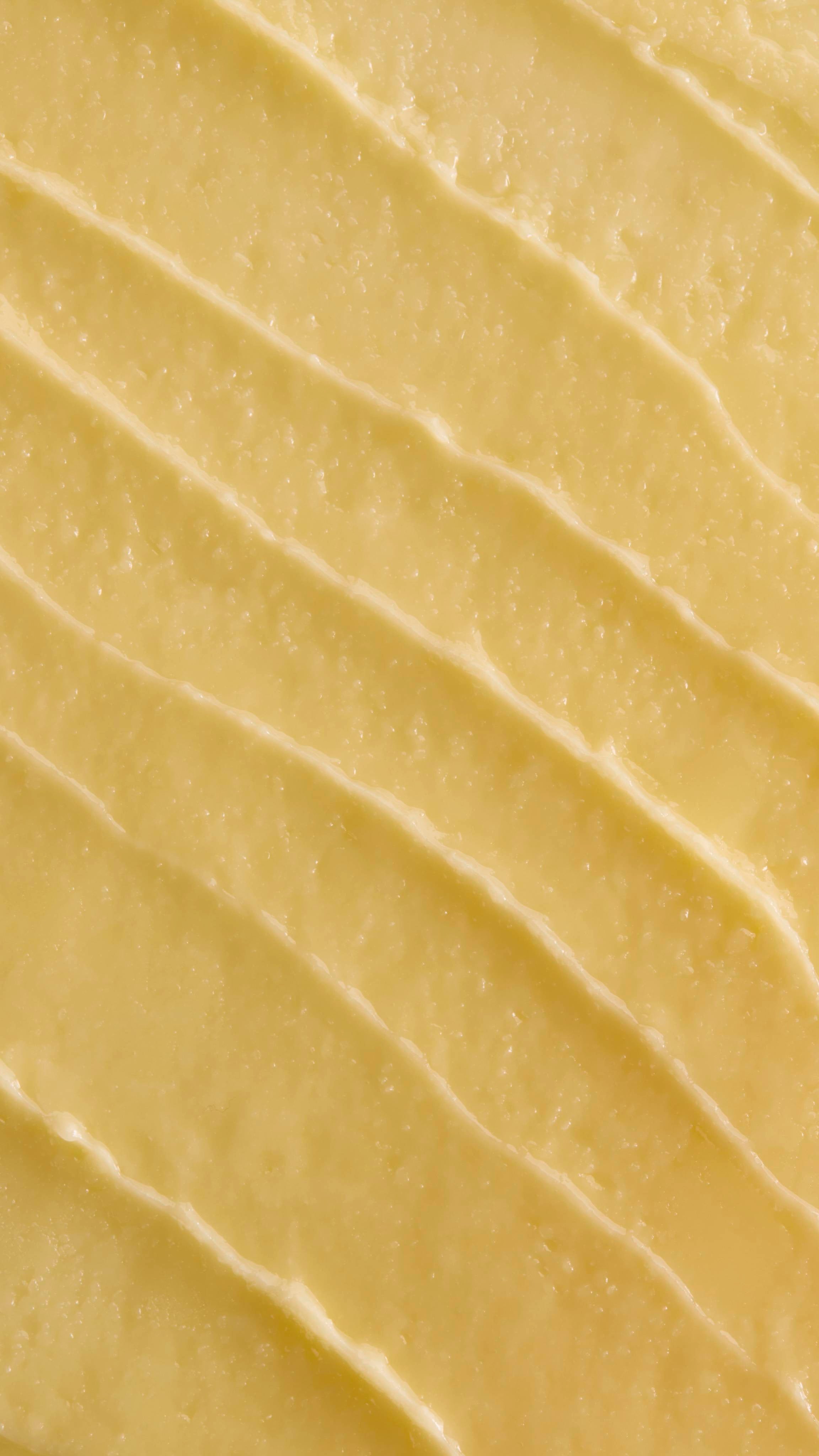 A close-up, aerial shot of thick, pale yellow 'Ultraplant' facial cleanser. The product is spread out in several diagonal, textured ridges, showing its smooth yet slightly granular, buttery consistency.
