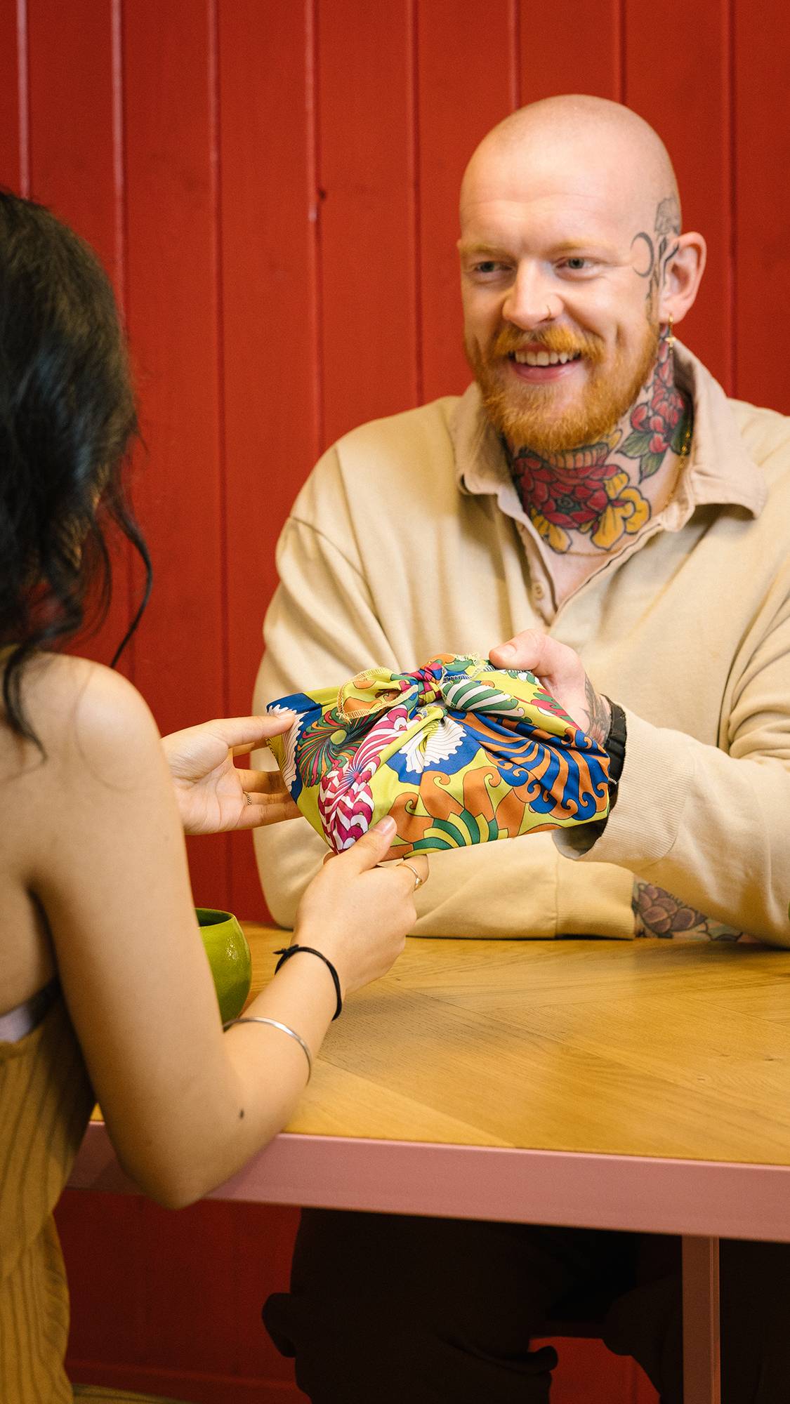 Image shows an exchange between friends where the gift is wrapped neatly in the colourful Whirly Swirly knot wrap.