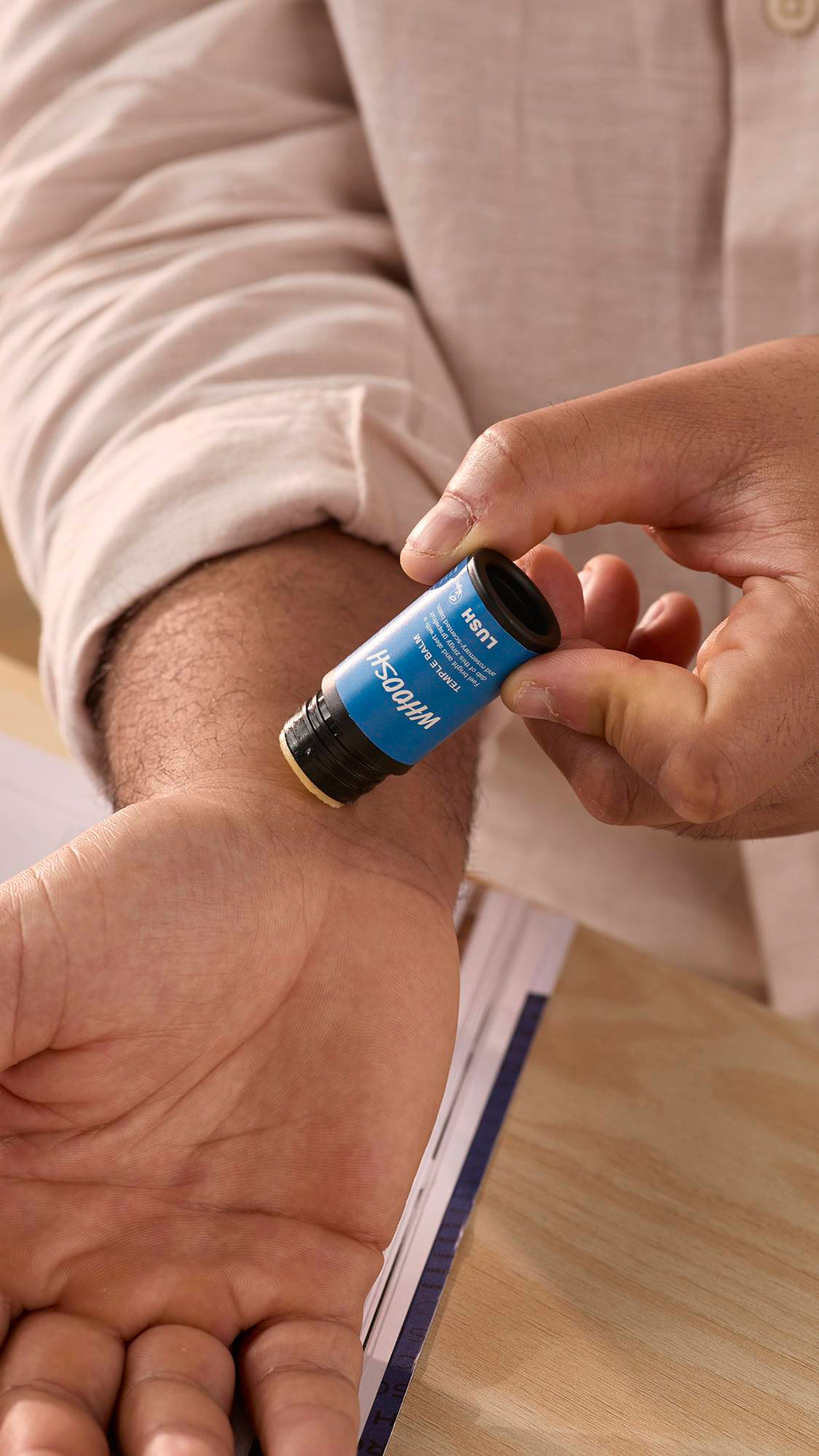 The image shows a close-up of the model's forearms and hands as they gently swipe the balm stick across their wrist.